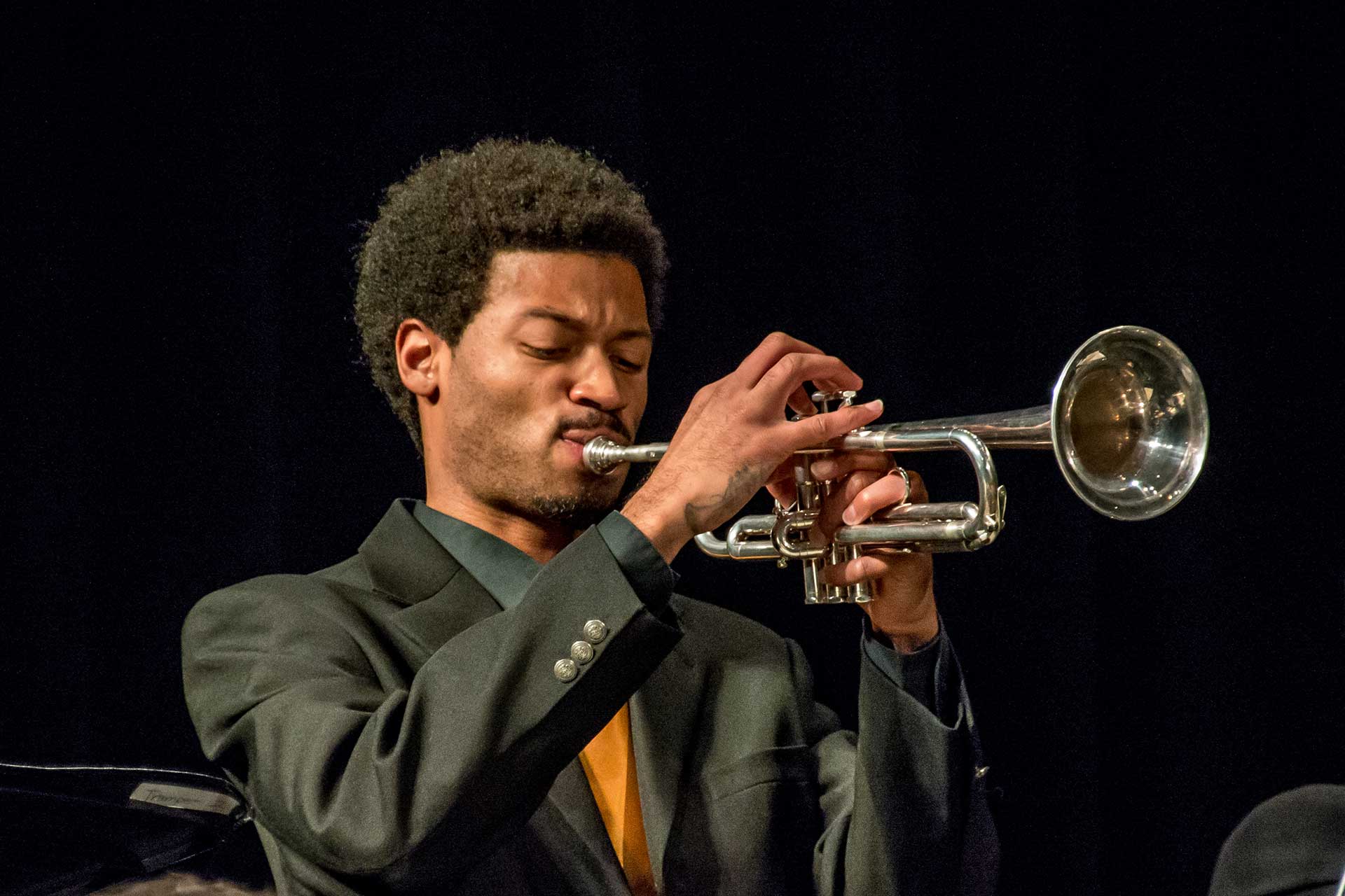 Photo of a trumpet player on stage infront of a back background