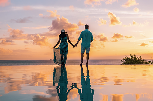Photo of a couple holding hands against a sunset sky.